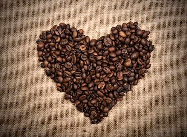 Fondo de granos de café en forma de corazón sobre fondo de arpillera