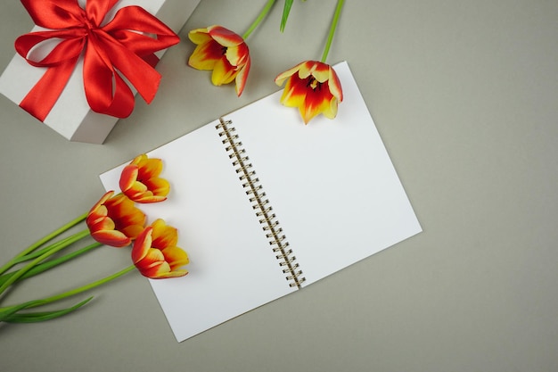En un fondo gris hay un cuaderno abierto para escribir y hay tulipanes rojos y amarillos.