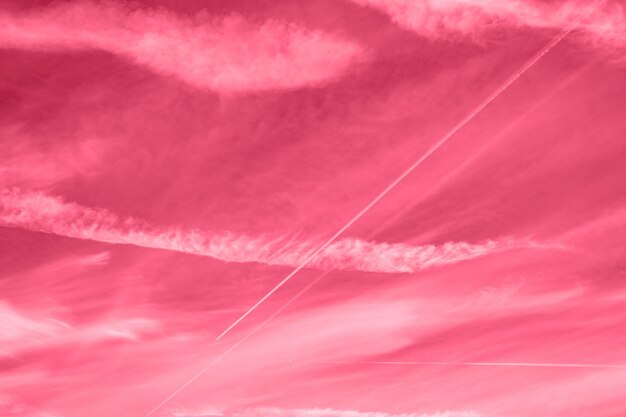 Fondo de un hermoso cielo de día púrpura rosa rojo brillante con cirros blancos y rastro desde el avión tonificado en el color de tendencia magenta viva del año 2023