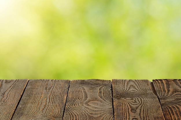 Fondo con hojas verdes borrosas y tablones de madera vacíos en primer plano