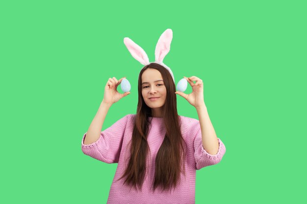 Fondo de huevos de Pascua descuentos de vacaciones y concepto de ventas Niña feliz en las orejas de conejo con huevos decorados sonriendo aislado sobre un fondo verde en el estudio