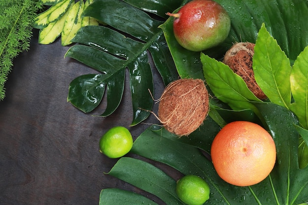 Fondo de madera oscura con hojas y frutas tropicales Vista superior plana mangos cocos y limas