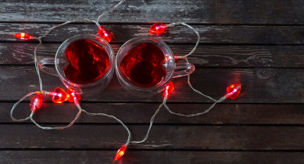 en un fondo de madera oscuro una taza de té en forma de corazón con té rojo y una guirnalda