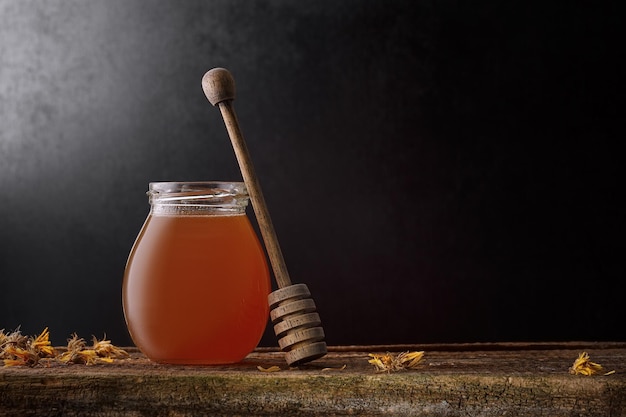 Fondo de miel. miel dulce en un frasco de vidrio y una cuchara de miel sobre la mesa .. fondo oscuro.