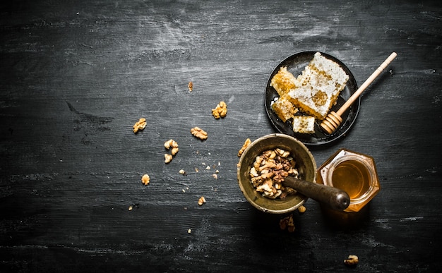 Fondo de miel. Nueces en un mortero y miel dulce en el panal. Sobre mesa rústica negra.