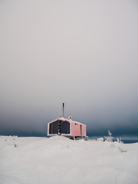 Fondo minimalista vertical con una cabaña roja solitaria en invierno bajo un cielo dramático Dubladom en la montaña Volodyanaya Kandalaksha Región de Murmansk en Rusia Copiar espacio