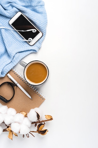Un fondo moderno de un suéter, una taza de café, un teléfono inteligente y una rama de algodón