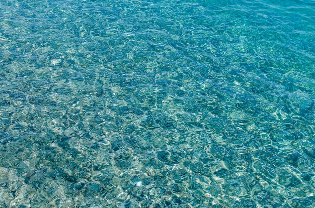 Fondo natural de agua clara de mar azul transparente. Fondo azul del mar Mediterráneo con pequeñas piedras. de cerca