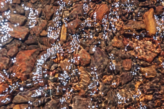 Fondo de naturaleza borrosa abstracta de corriente de agua clara con fondo pedregoso abigarrado a la luz del sol Textura de arroyo de montaña desenfocada en sol brillante Patrón borroso de piedras multicolores iluminadas por el sol en agua de manantial