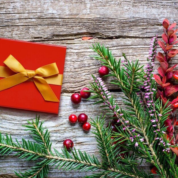 Fondo de Navidad con abetos brezos y flores silvestres y bayas en el fondo de madera vieja. Regalo en caja roja. Tonificación retro.