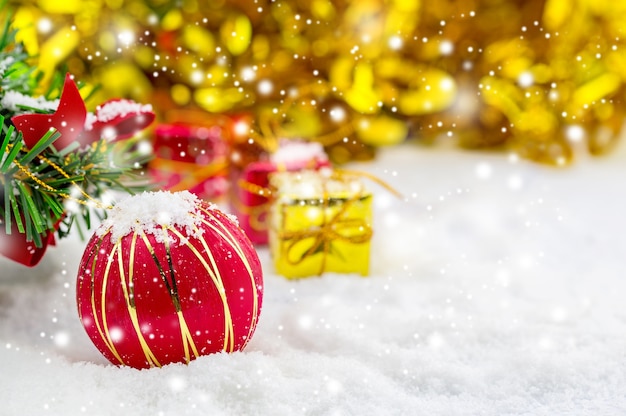 Fondo de Navidad con un adorno rojo, caja de regalo de oro en la nieve