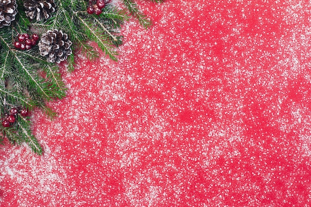 Fondo de Navidad y año nuevo, ramas de abeto verde y frutos rojos con nieve sobre un fondo rojo.