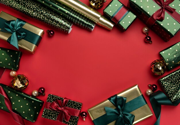Fondo de Navidad con cajas de regalo, cintas de raso y rollos de papel de regalo sobre fondo rojo.