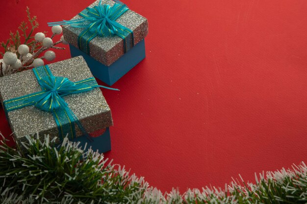 Fondo de navidad con cajas de regalo con lazo azul, ramas verdes y fondo rojo.
