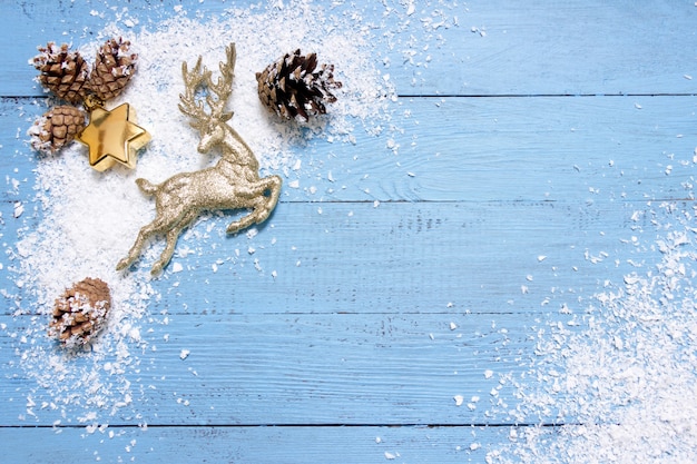 Fondo de Navidad-ciervos con purpurina dorada, estrellas y conos de abeto en la nieve, tablero de madera azul, tarjeta de felicitación