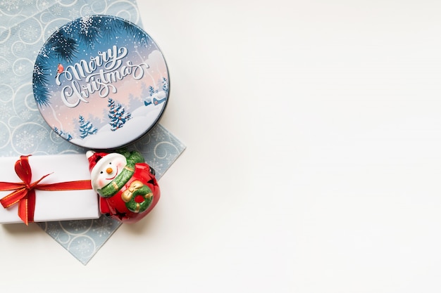 Fondo de Navidad con composición decorativa de caja de navidad, muñeco de nieve de cerámica, caja de regalo y servilleta azul claro. Feliz año nuevo. Copyspace