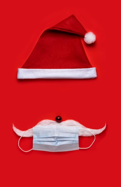 Fondo de Navidad de coronavirus. Sombrero de Papá Noel con mascarilla sobre un fondo rojo.