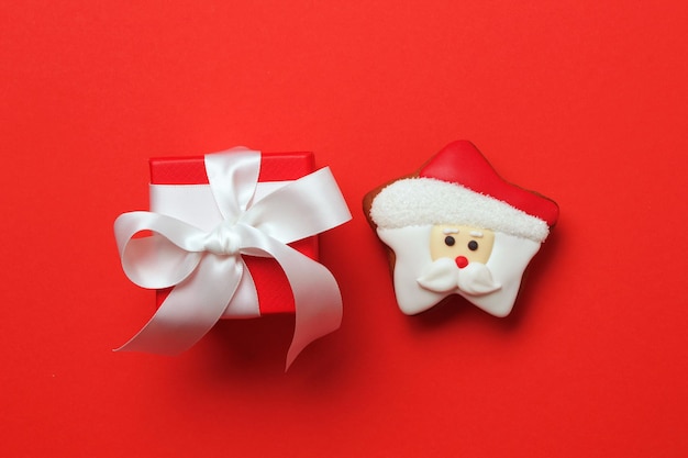 Fondo de navidad con galletas de hombre de jengibre de santa claus con caja de regalo roja sobre un fondo rojo plano