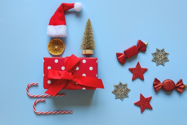 Fondo de Navidad con gorro de Papá Noel, caja de regalo, especias secas, anillos de naranja, canela, dulces, trineo