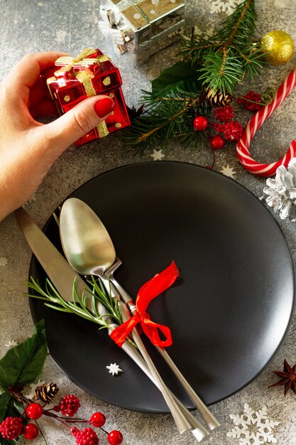 Foto fondo de navidad mesa de decoración navideña mano femenina sirve mesa festiva plato negro