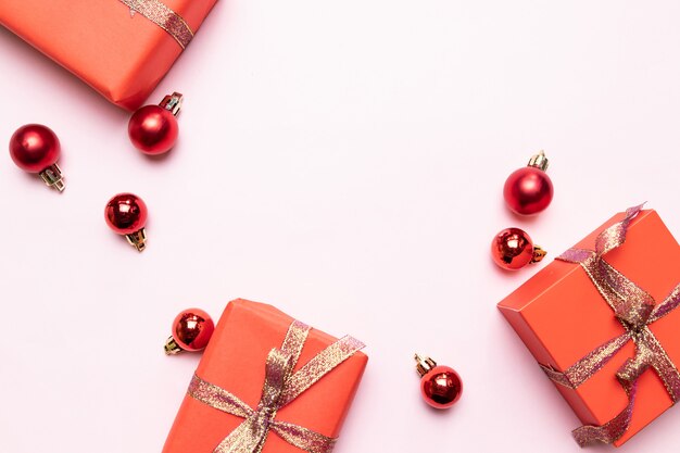 Fondo de Navidad de pequeños regalos rojos con cinta dorada, bolas sobre fondo rosa. Concepto mínimo de año nuevo.