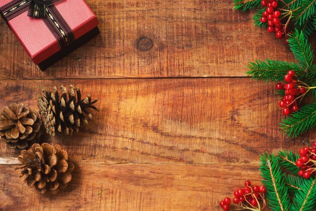 Fondo de Navidad. Ramas de abeto, regalo, piñas, frutos rojos sobre un fondo de madera. Vista superior. Tarjeta de Navidad o año nuevo. Lugar para texto, plano