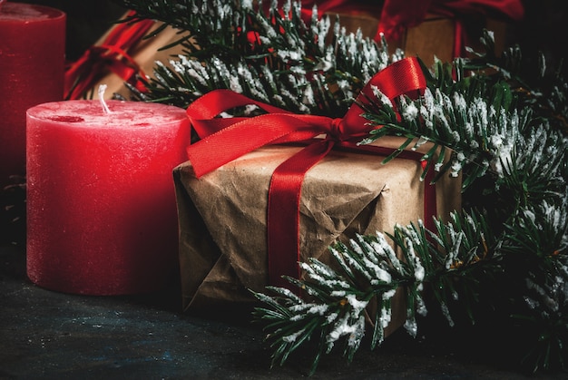 Fondo de Navidad para tarjeta de felicitación. Ramas de los árboles de Navidad con efecto de nieve con cinta roja festiva, piñas, cajas de regalo y velas, sobre fondo azul oscuro
