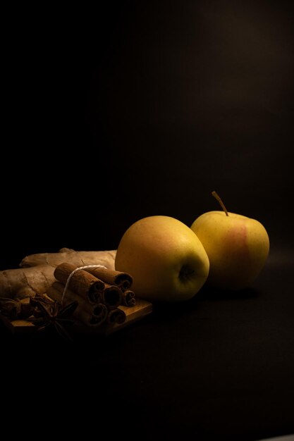 Foto un fondo negro con dos manzanas y palitos de canela.