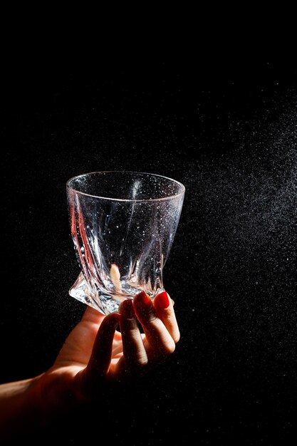 El fondo negro es un primer plano de un vaso limpio en una mano. Pulverizar sobre un vaso de agua. Vidrio aislante