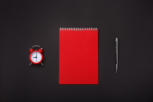 Fondo negro rojo alarma reloj libreta bolígrafo espacio en blanco escritorio