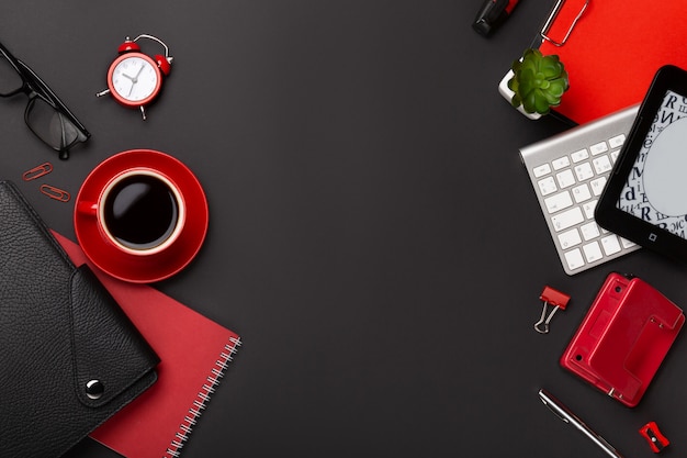 Fondo negro con taza de café roja, bloc de notas, reloj despertador y flores en la vista superior