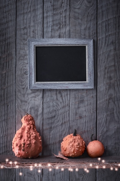 Fondo de noche de otoño con marco de pizarra en pared de madera rústica, calabazas decorativas naranjas y luces de guirnalda, espacio de copia