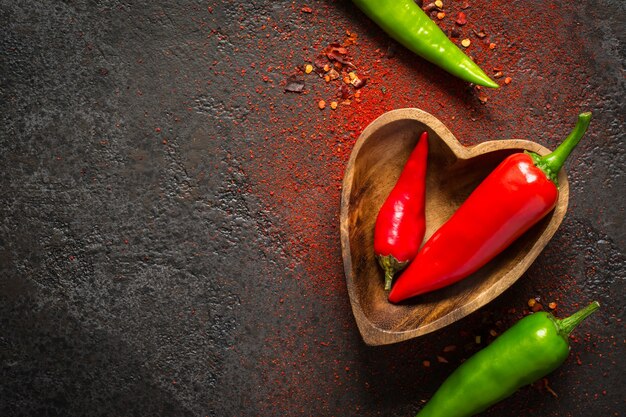 Fondo oscuro de la comida de las especias. Pimiento rojo y verde en un cuenco de madera.