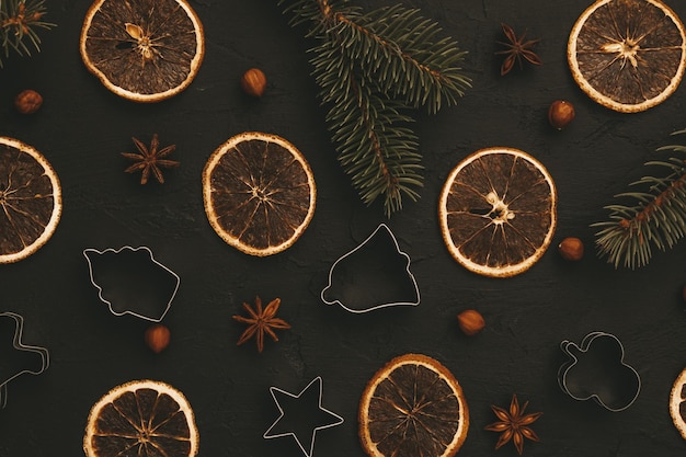 Fondo oscuro de la comida de Navidad. Ramas de abeto con cortadores de galletas, chips de naranja secas, anís, especias de invierno y nueces. Vista superior. Composición culinaria. Tarjeta navideña para el año nuevo 2022. Lay Flat.