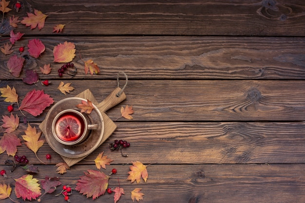 Fondo de otoño con espacio de copia. Té con limón, hojas y bayas en una mesa de madera.