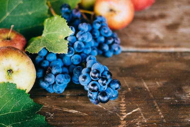 Foto el fondo del otoño con las manzanas, la uva y la uva se va en un viejo fondo de madera. otoño