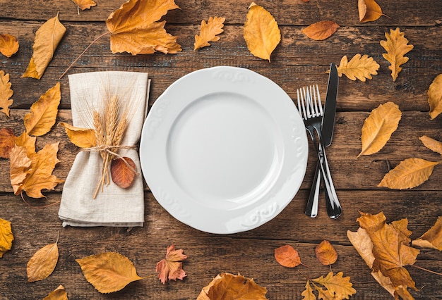 Fondo de otoño con una servilleta de plato y cubiertos sobre un fondo de madera con hojas