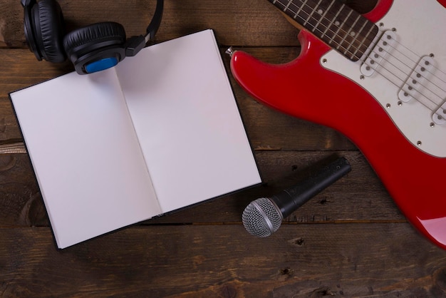 Foto fondo de pantalla de guitarra con micrófono, auriculares, cables y fondo de madera, con bloc de notas