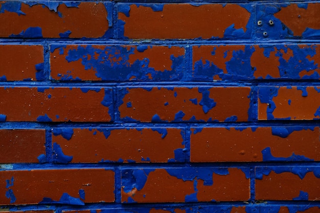 Fondo de pared colorido con pinturas dañadas de azul sobre ladrillos rojos