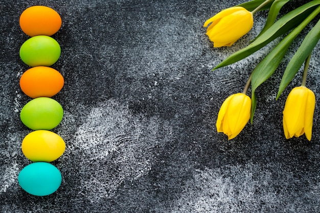 Fondo de Pascua con espacio de copia. Tarjeta de regalo pascual con huevos pintados y tulipanes amarillos sobre fondo negro oscuro grunge.