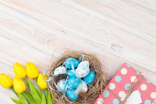 Fondo de pascua con huevos azules y blancos en nido de tulipanes amarillos y caja de regalo