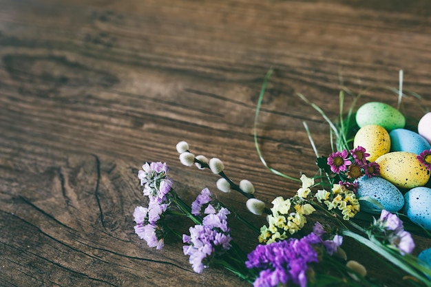 Fondo de Pascua huevos de colores brillantes en el nido con flores de primavera sobre fondo oscuro de madera selec