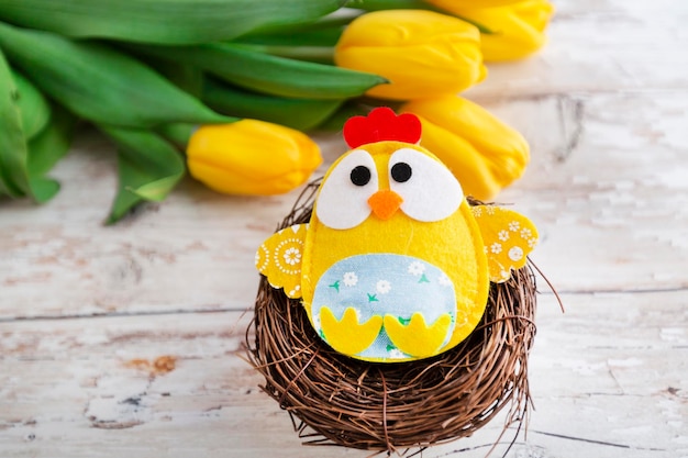 fondo de pascua con pollo decorativo en nido y tulipanes amarillos sobre fondo de madera