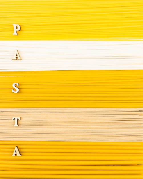 Un fondo de pasta larga seca, fideos y espaguetis con una palabra de pasta de letras de madera. vista superior. endecha plana.