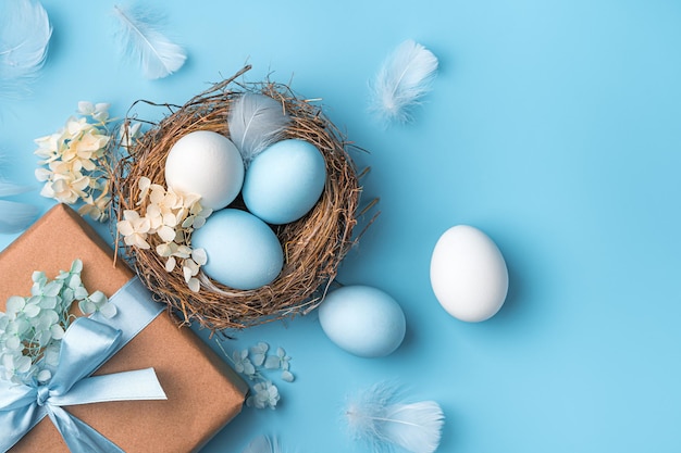 Fondo pastel de Pascua con huevos, un nido y un regalo sobre un fondo azul El concepto de un espacio de copia de feliz Pascua Vista superior