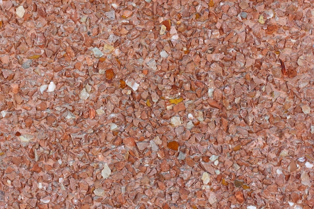 Fondo pequeñas piedras rojas y anaranjadas en el yeso en la pared, estructura uniforme.