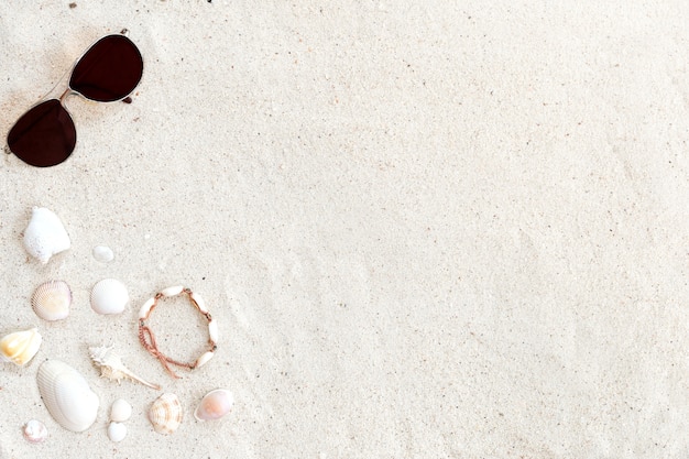 Fondo de playa. Playa de arena con gafas de sol, conchas y pulsera hecha de conchas marinas.