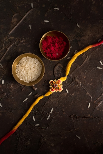 Fondo de Raksha Bandhan con un elegante Rakhi, granos de arroz y Kumkum