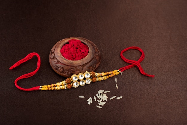 Fondo de Raksha Bandhan con un elegante Rakhi, granos de arroz y Kumkum