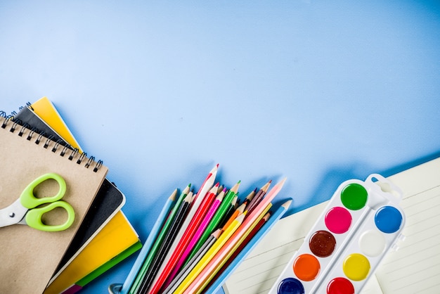 Fondo de regreso a la escuela con accesorios para el aula: pinturas, lápices, cuadernos, libros, tijeras, tiza, marcadores, fondo azul, espacio de copia superior